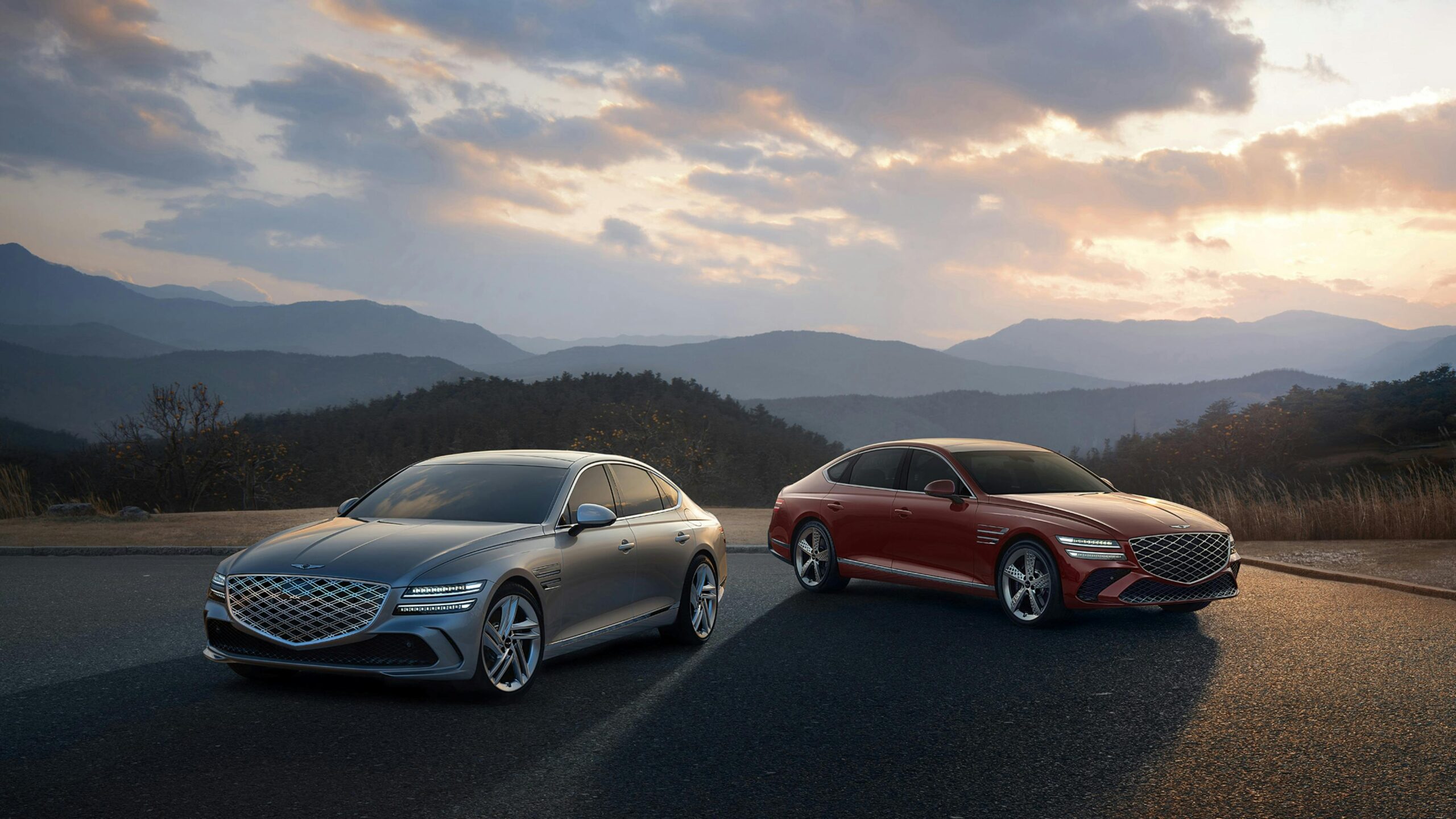 Two luxury sedans parked with a stunning mountain backdrop at sunset.